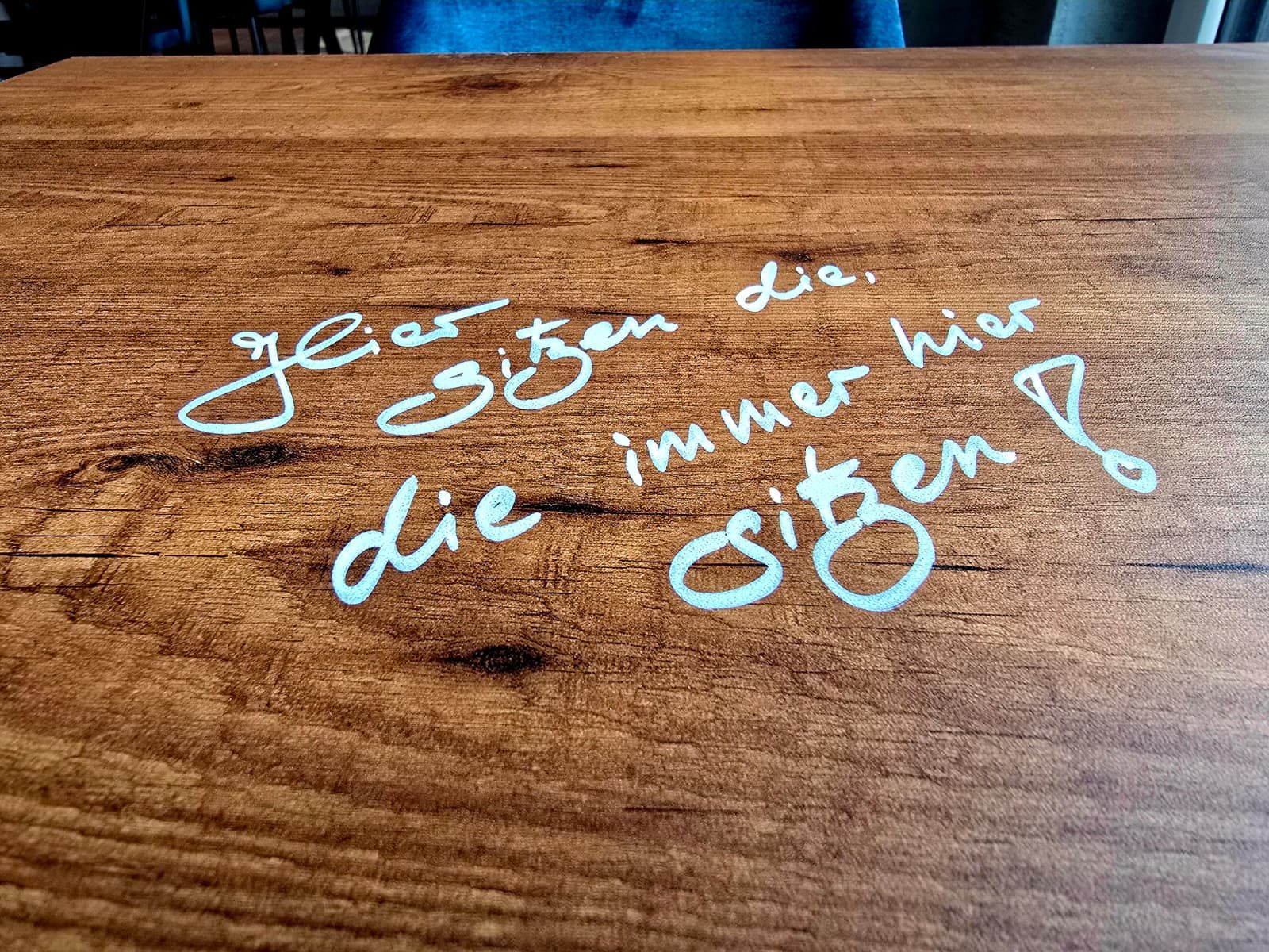 Tischplatte mit Schriftzug: Hier sitzen die, die immer hier sitzen!